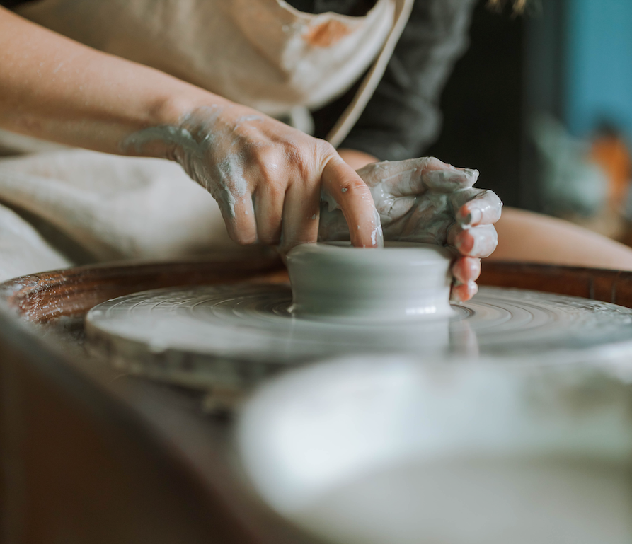 Hands opening mound of clay on a pottery wheel.